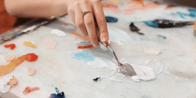 Hand using a Palette Knife with many colored paints on the pallet